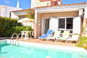 A pool area with a clear pool, a table with an umbrella, and several lounge chairs.
