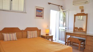 A bedroom with a bed, a nightstand, a desk, a chair, a mirror, and a door leading to a balcony.