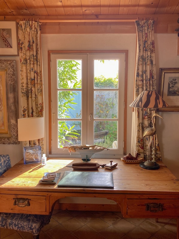 A wooden desk with a window, a lamp, and a framed picture.