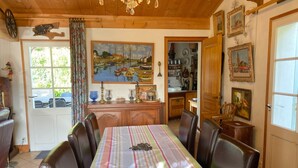 A dining area with a long table, chairs, and a painting of boats on the wall.