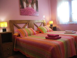 Ein Doppelbett mit farbenfroher, gestreifter Bettdecke und Kissen, zwei Nachttische mit Lampen, ein Gemälde an der Wand und ein Fenster mit Vorhängen.