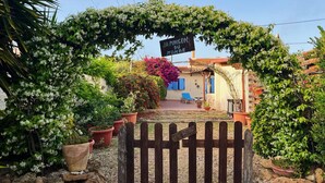 A rustic villa with a wooden gate, surrounded by lush greenery and flowering plants.