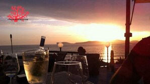 A sunset view from a terrace with a table set for dining, glasses of water, and a bottle.