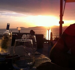 Vista del atardecer desde una terraza con una mesa dispuesta para comer, vasos de agua y una botella.