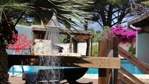 A pool area with a water feature, wooden deck, and a view of a building with a tiled roof.