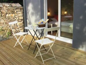 Une terrasse extérieure avec un mur en pierre, une plateforme en bois et une porte vitrée donnant sur l’intérieur.