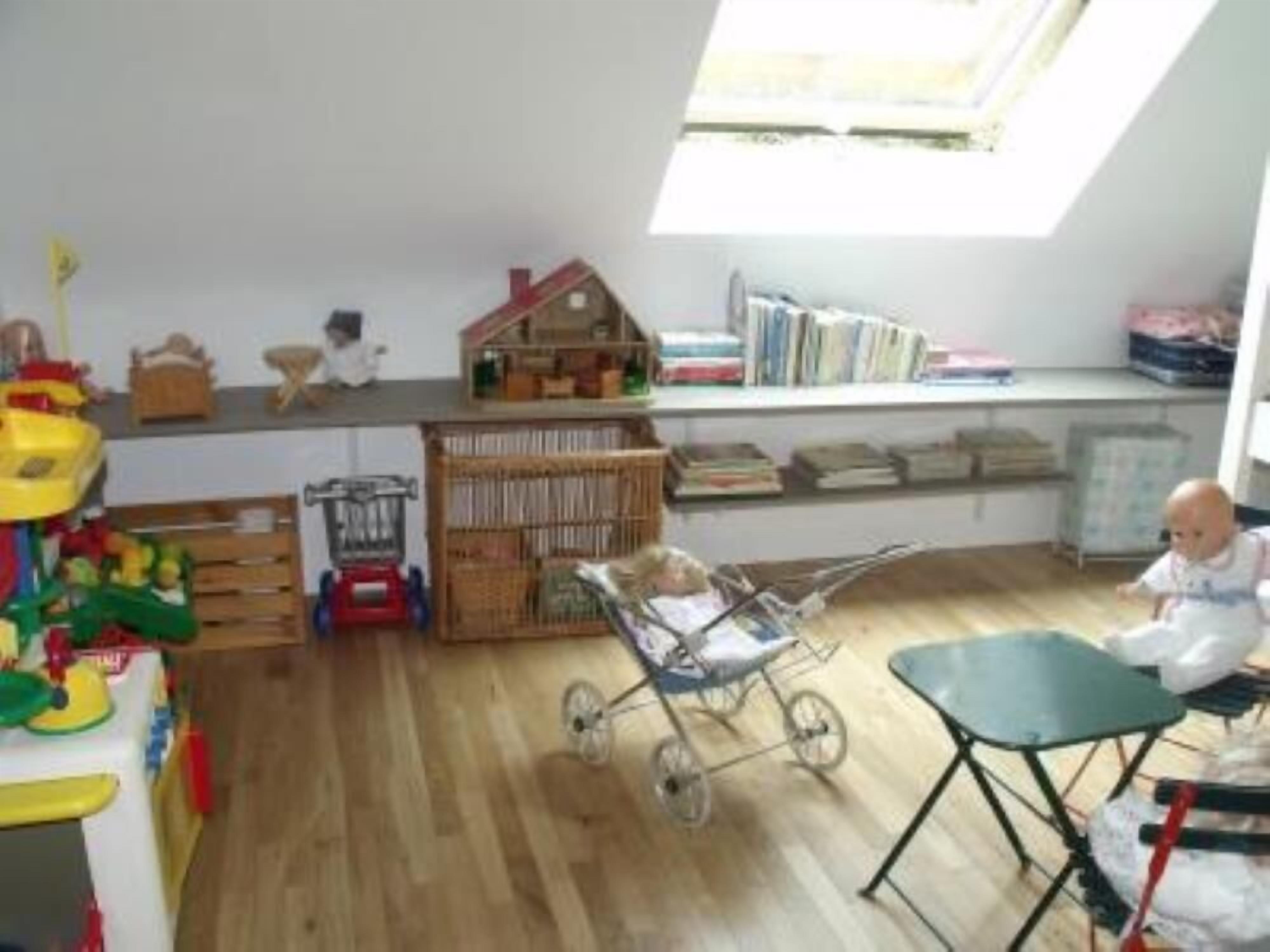 A room with a skylight, a crib, a stroller, and a table with a chair.