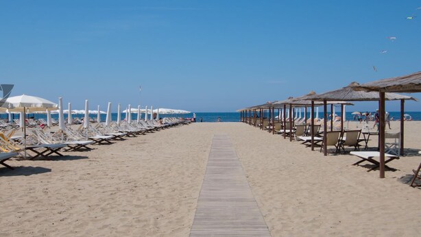 Une plage bordée de rangées de chaises longues et de parasols, une promenade en bois et, au loin, d’autres parasols de plage.