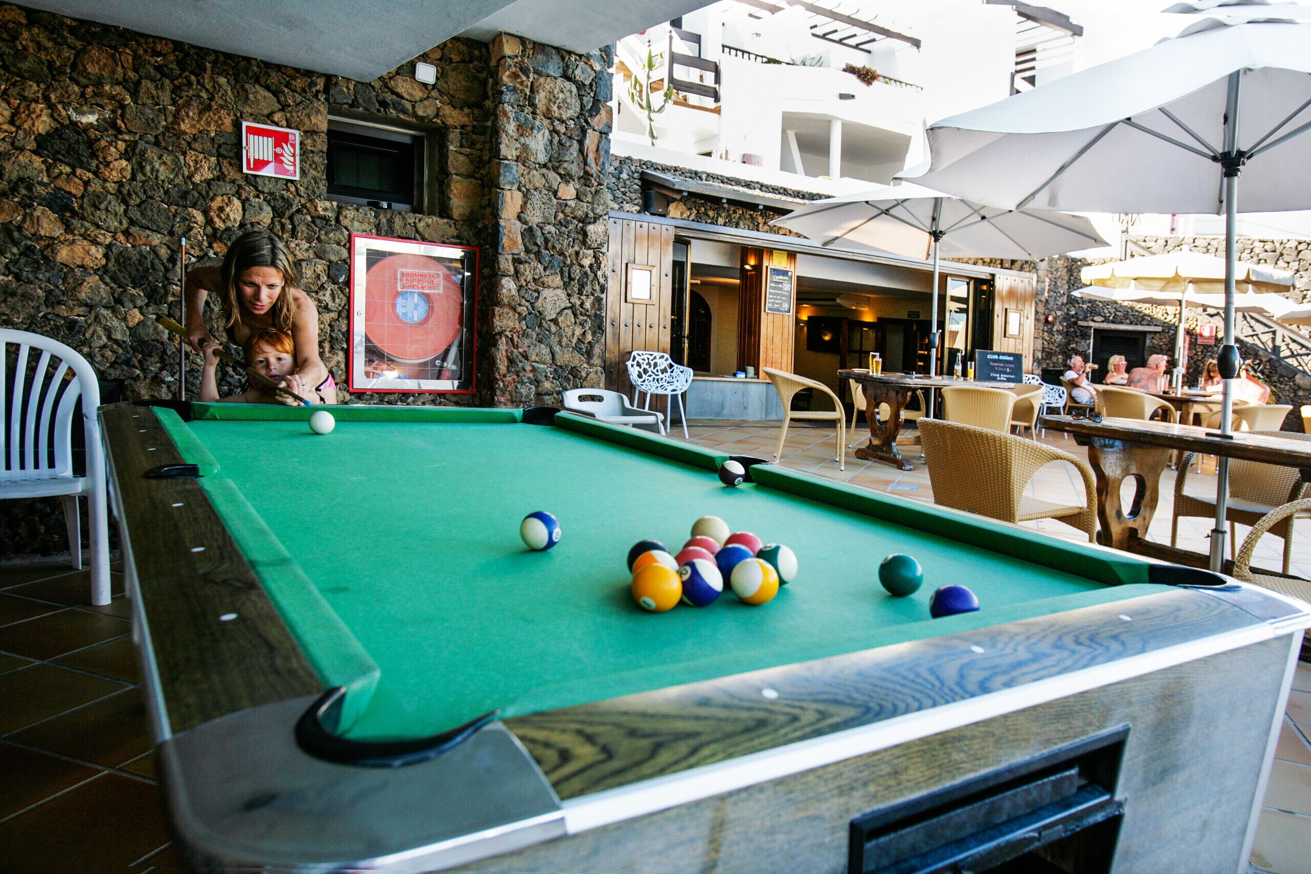 A pool table with balls, a stone wall, and outdoor seating with umbrellas.