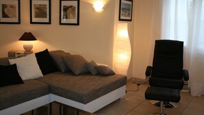 Una sala de estar con un sofá, un sillón, una lámpara y cuadros enmarcados en la pared.
