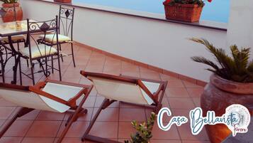 A terrace with a table and chairs, potted plants, and a view of the sea.
