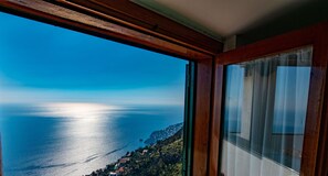 Une vue depuis une fenêtre donnant sur une ville côtière, avec une enseigne indiquant « Casa Bella Vista ».