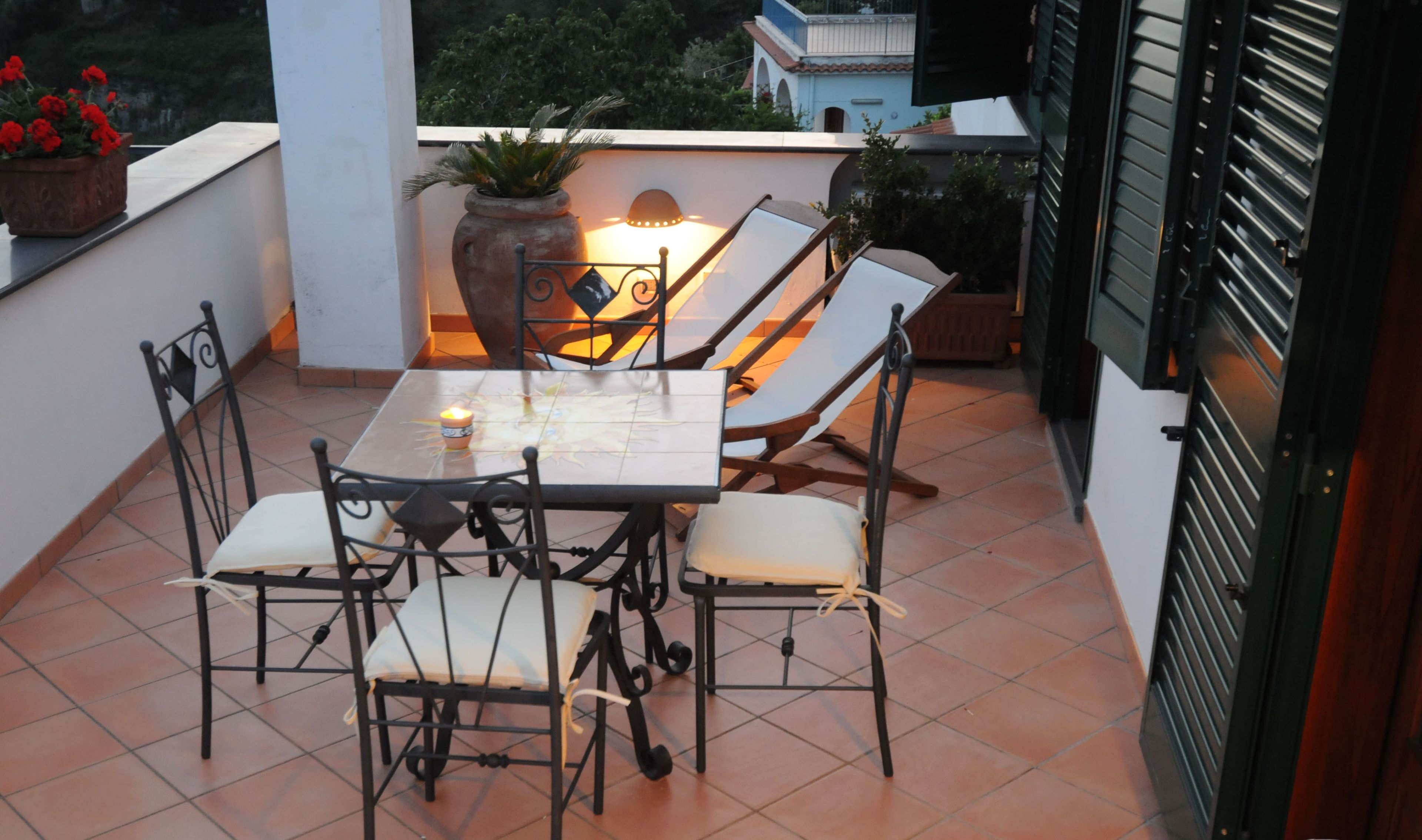 Eine Terrasse mit Tisch, Stühlen, einer Topfpflanze und einer Lampe.