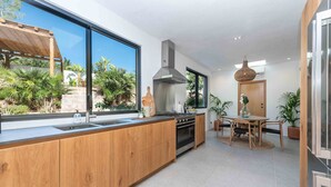 Una cocina moderna con un gran ventanal, armarios de madera, horno empotrado y un comedor con mesa y sillas.