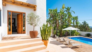 Una villa moderna con piscina, terraza de madera y una escalera que conduce a la entrada.