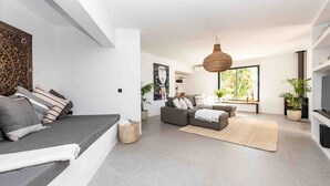 Una sala de estar moderna con un sofá gris, un sofá cama gris y una lámpara colgante grande de tejido. Hay plantas en macetas y un televisor de pantalla plana sobre un mueble.