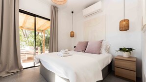 Un dormitorio moderno con una cama grande, una mesita de noche con una planta y vistas al exterior a través de una puerta corrediza de vidrio.