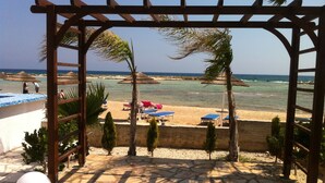 Vista a la playa con una pérgola de madera, sillas de descanso y sombrillas.
