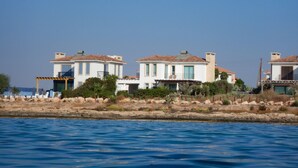 Una propiedad costera con tres edificios blancos, cada uno con tejado de baldosas y un balcón. La propiedad está situada frente al mar, con un litoral rocoso en primer plano.