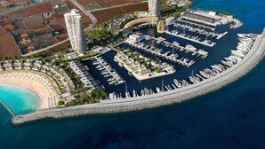 Vista aérea de una marina costera con varios muelles, un edificio central y una zona de playa.