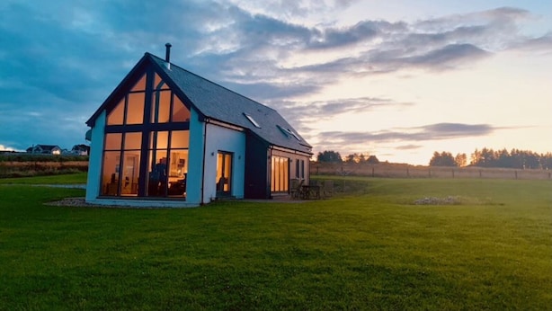 Une maison moderne dotée de grandes fenêtres, d’un toit en pente et d’une pelouse bien entretenue.