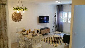 A dining area with a wooden clock, a television, and a dining table set with plates and candles. - Enchanted land of Asturias (Gijón)