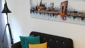 A living room with a black sofa, teal and mustard cushions, a round coffee table, and a cityscape painting on the wall. - Enchanted land of Asturias (Gijón)