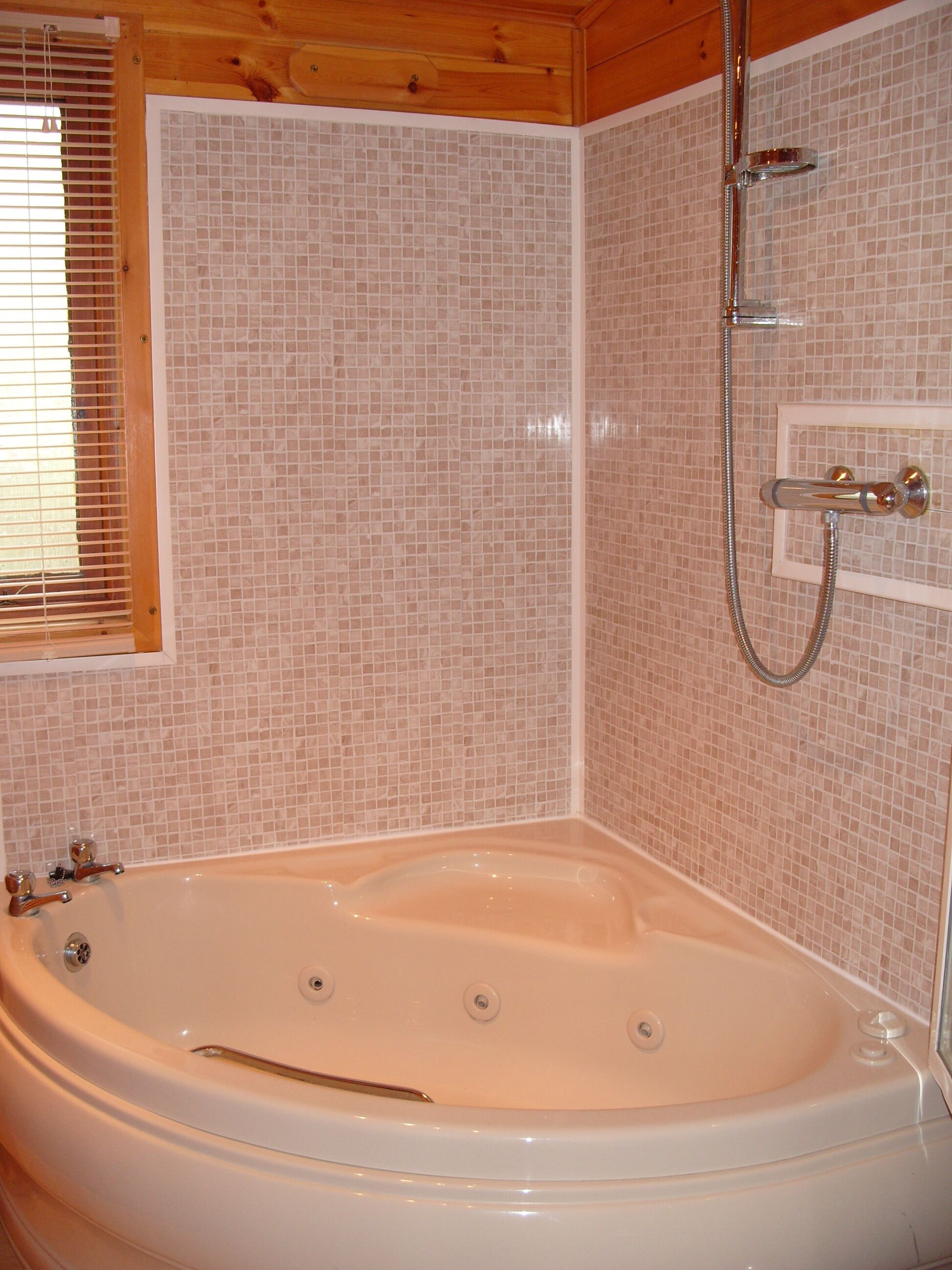 Een badkamer met een vrijstaand bad, een douche met een handdouche en een raam met zonwering.