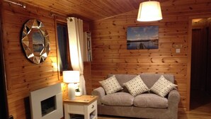 A cozy room with wooden walls, a grey sofa with patterned cushions, a round rug, and a mirror on the wall. - Lake District Log Cabin (Troutbeck Bridge)