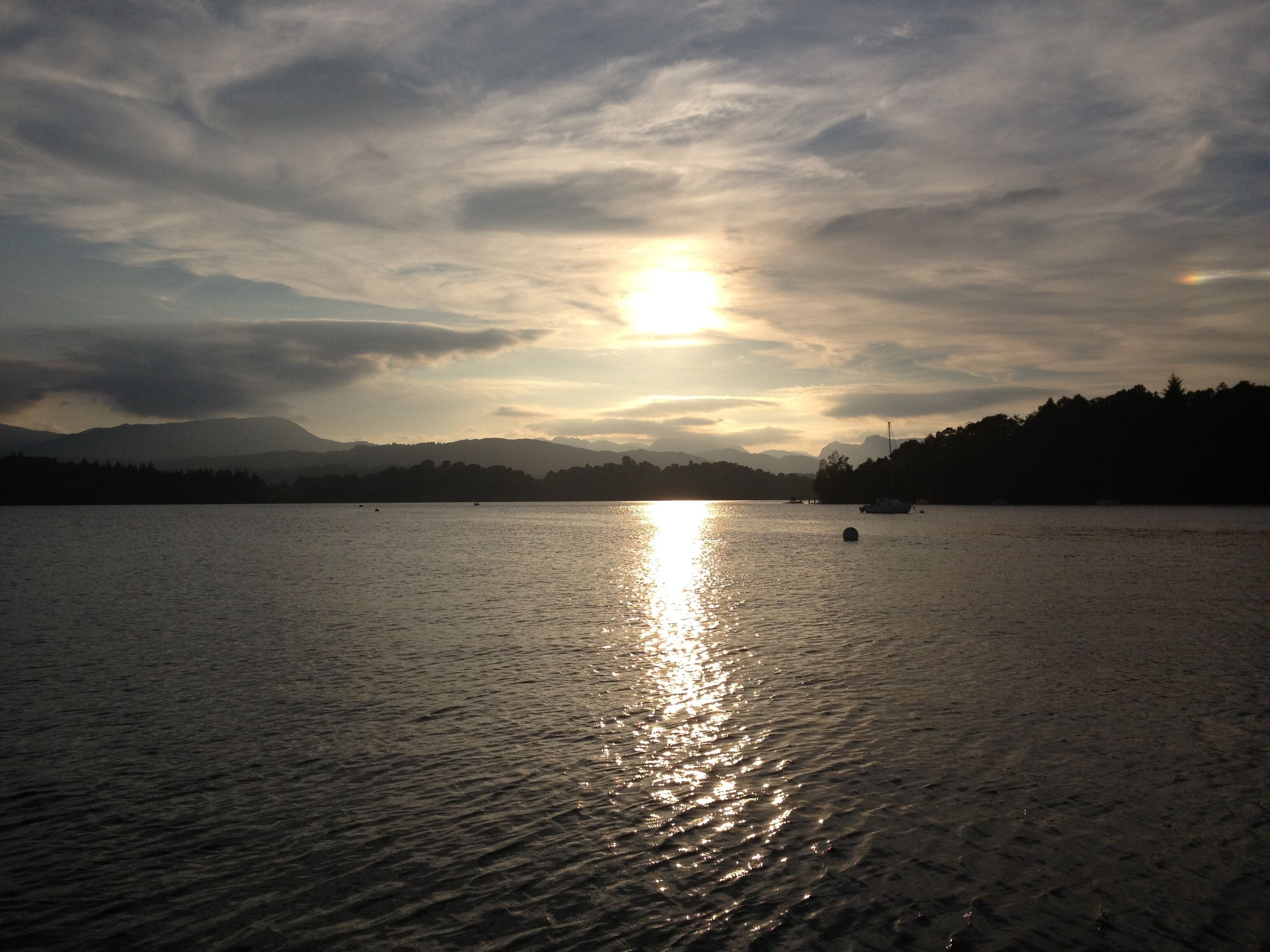 A calm lake with a sunset reflecting on the water, surrounded by mountains and trees.