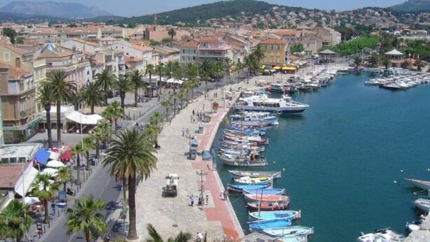 A coastal town with a marina, buildings along the waterfront, and palm trees lining the streets.