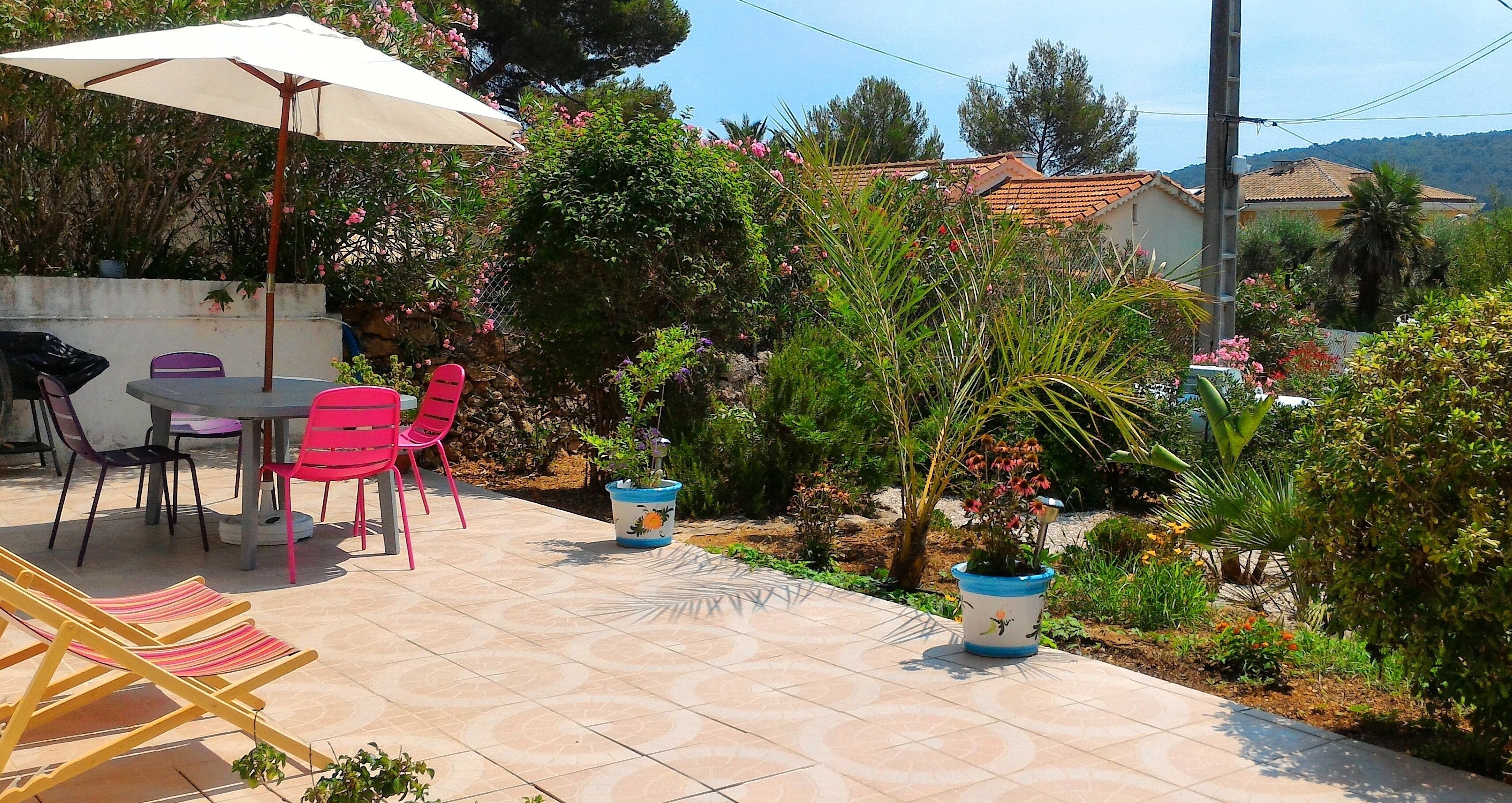 Eine Terrasse im Freien mit Tisch und Stühlen, umgeben von Topfpflanzen und einem gefliesten Boden.