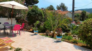 An outdoor patio with a table and chairs, surrounded by potted plants and a tiled floor.