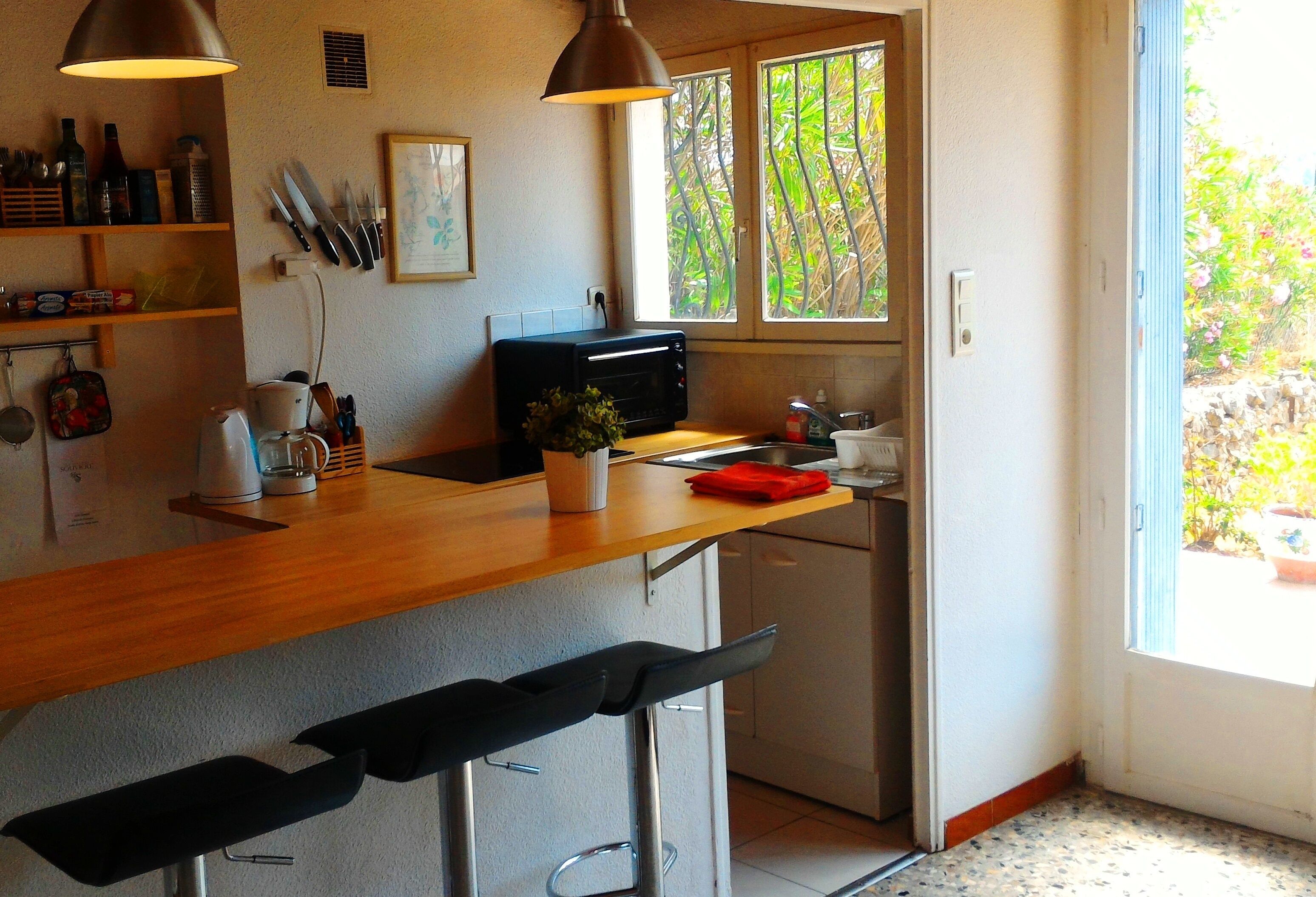 A kitchen with a wooden countertop, a coffee maker, a toaster, and a sink. There are two bar stools and a window with a view of greenery.
