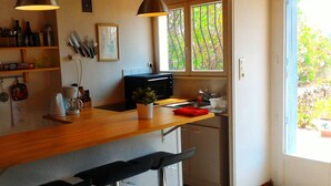 A kitchen with a wooden countertop, a coffee maker, a toaster, and a sink. There are two bar stools and a window with a view of greenery.