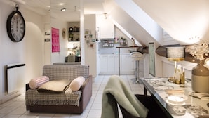 A cozy living room with a patterned sofa, a dining table with a vase, and a kitchen in the background. - Studio With a Nice View of Paris - Luxury Building in the Heart of the Marais (Paris)