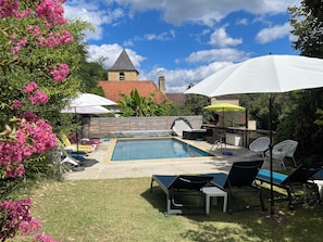 Un patio trasero con piscina, sillas de descanso, sombrillas y una pequeña mesa.