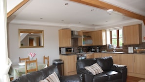 A spacious living area with a black leather sofa, a dining table with chairs, and a kitchen with wooden cabinets and modern appliances. - Rural Cotswold Cottage in grounds of beautiful Nell House (Hannington)