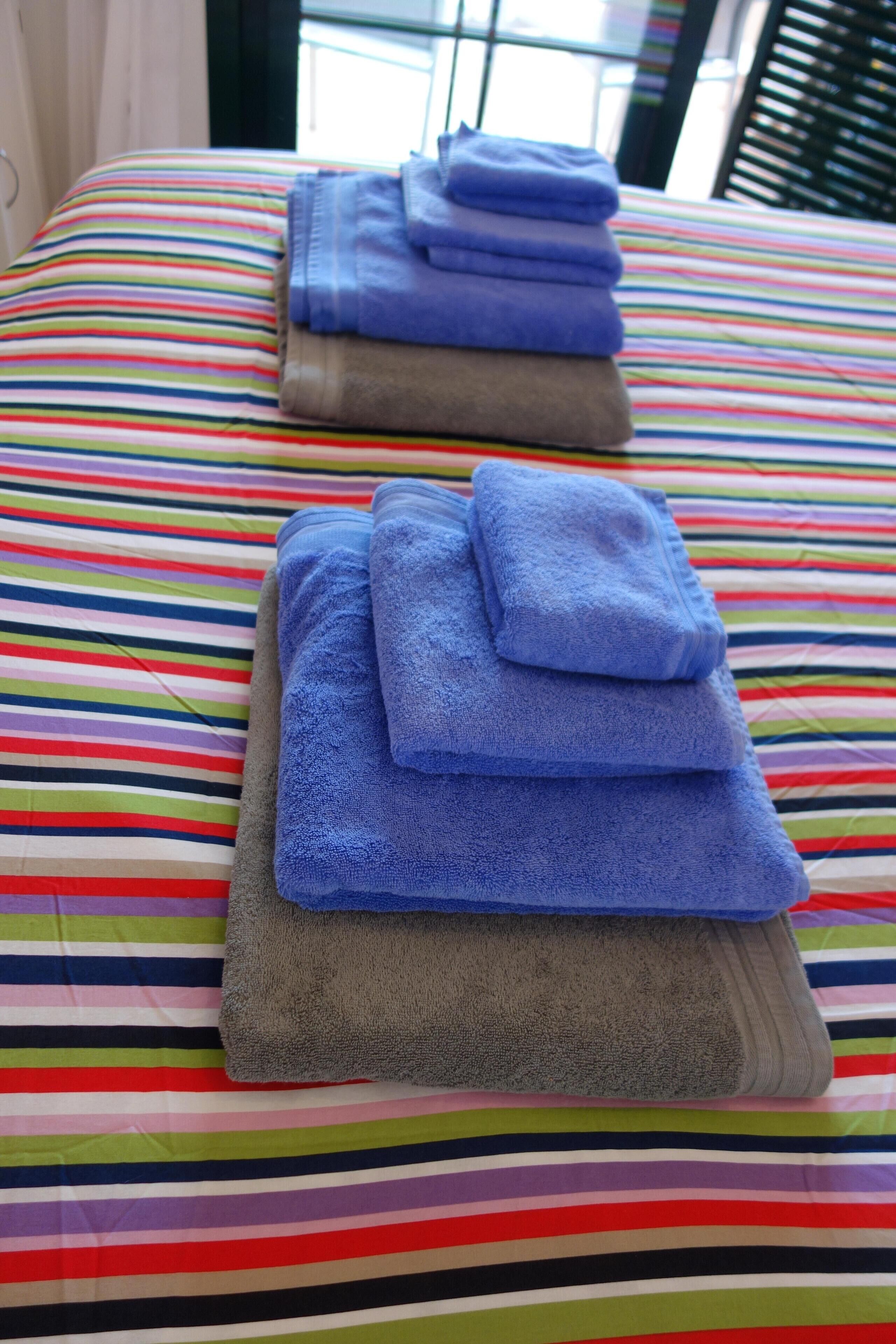 Ein Bett mit einer bunten, gestreiften Bettdecke und ordentlich gefalteten Handtüchern in Blau und Grau.