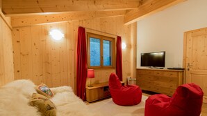 Habitació acollidora amb parets i sostre de fusta, una finestra amb cortines, televisió, una butaca de plàstic vermella i una catifes blanca i esponjosa.