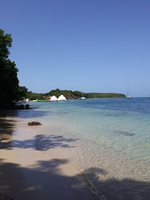A beach with clear water, boats, and a distant island.