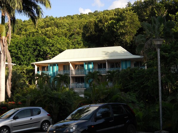 A two-story building with a flat roof, surrounded by lush greenery and palm trees.