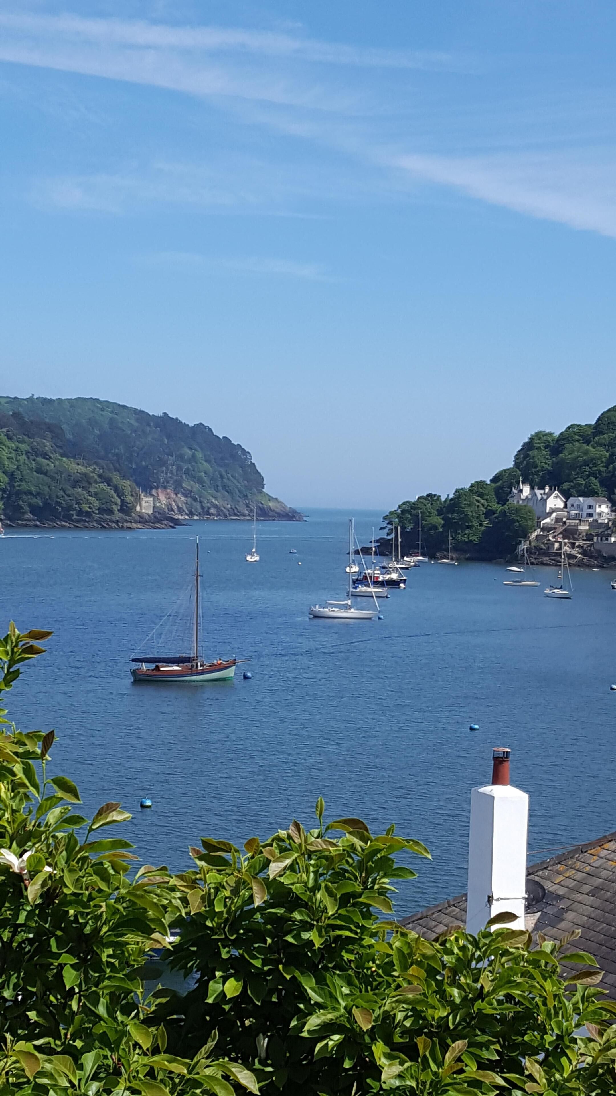 A coastal scene with boats on calm waters, greenery, and buildings on the hills.