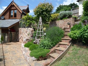 A wooden house with a stone wall and a wooden ladder leading to a garden. - Charming Character Cottage in Picturesque Village 5 * rated.  (Newton Abbot)