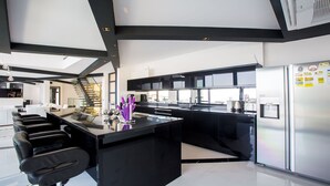 A modern kitchen with a central island, black cabinetry, stainless steel appliances, and a staircase leading to an upper level. - Villa Tyra ultra modern luxury 5 bedroom villa with stunning sea views (Kalkan, Kas)
