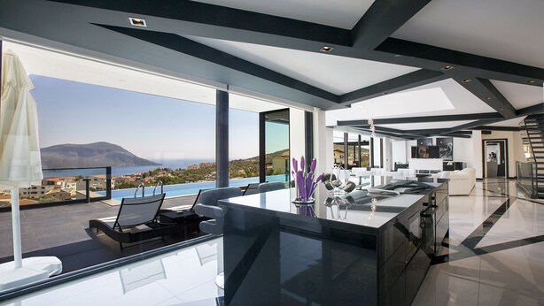 A modern kitchen with a large island, a dining area with a view of the sea, and a spacious living area with a staircase. - Villa Tyra ultra modern luxury 5 bedroom villa with stunning sea views (Kalkan, Kas)