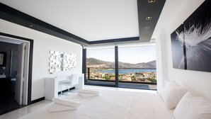 A modern bedroom with a large window, a white bed, and a view of a coastal town. - Villa Tyra ultra modern luxury 5 bedroom villa with stunning sea views (Kalkan, Kas)