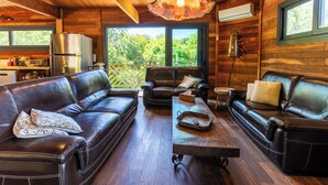 A cozy living room with leather sofas, a coffee table, and a large window offering a view of greenery. - House / Villa - Porto vecchio (Porto-Vecchio)