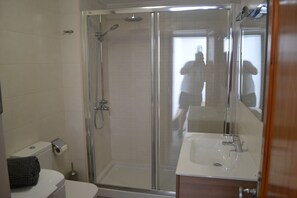 Un baño con ducha de vidrio, lavamanos blanco y retrete.