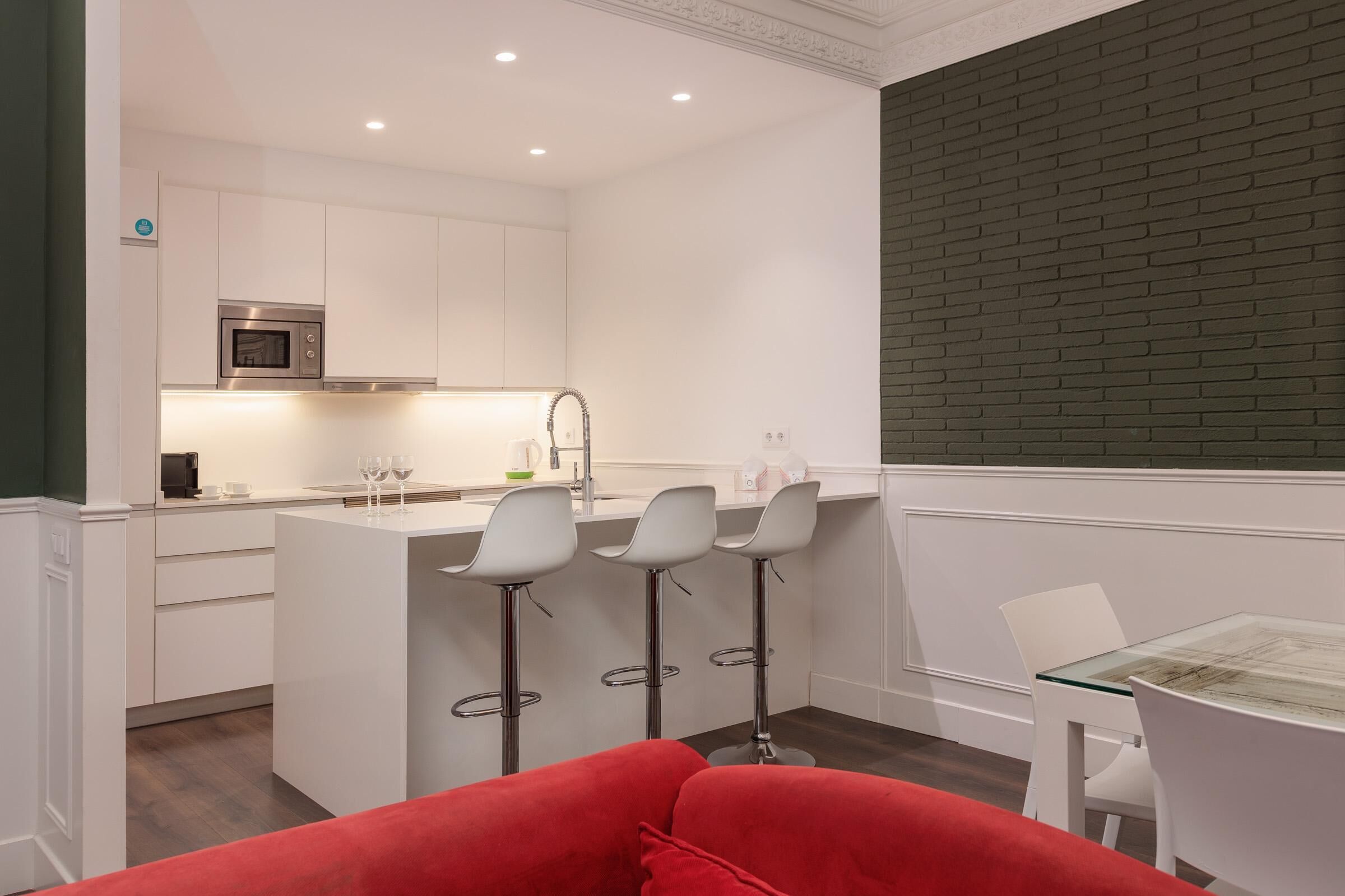 A modern kitchen with white cabinetry, a stainless steel microwave, and a bar area with stools.